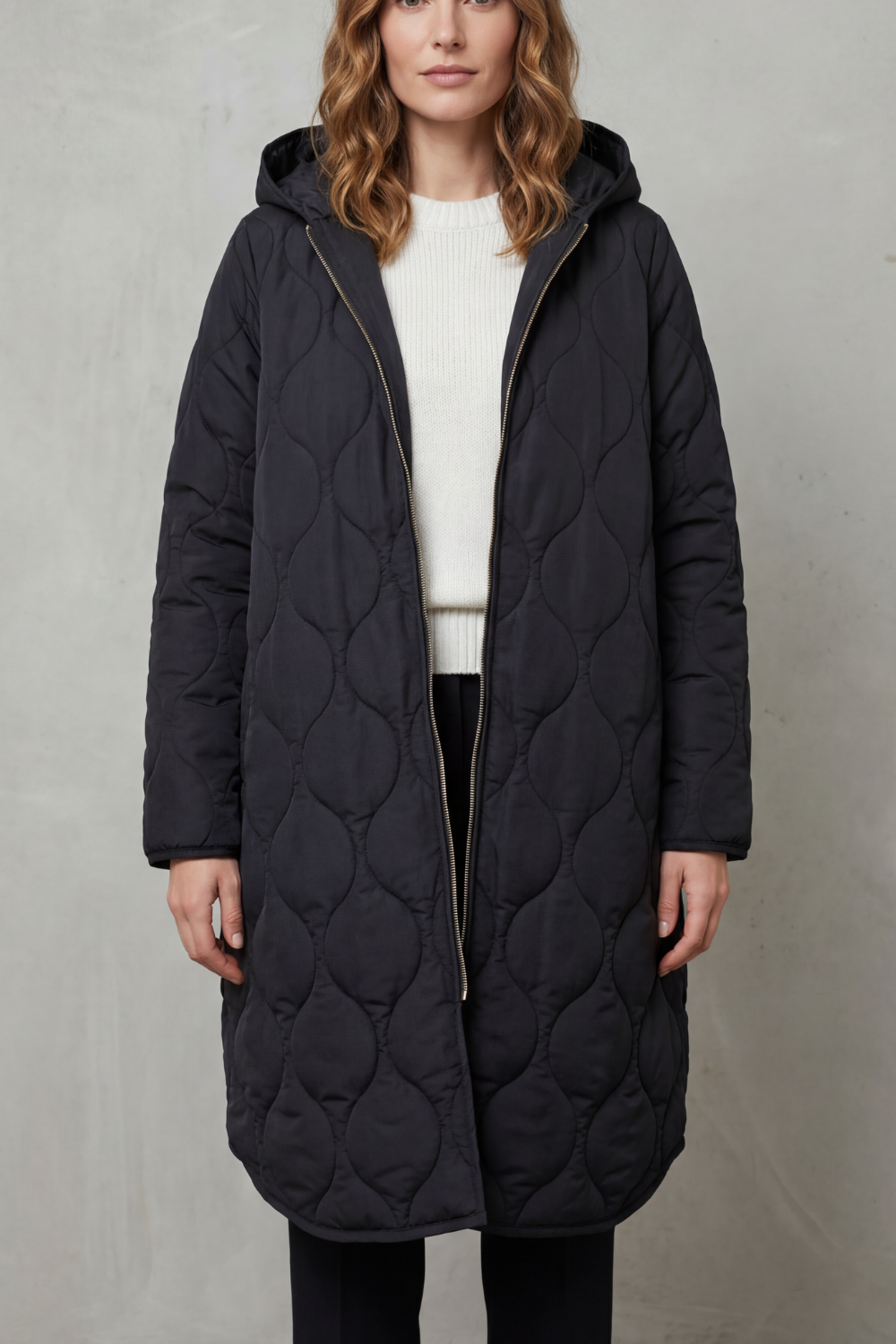 Modella indossa un parka trapuntato lungo con cappuccio, zip frontale e vestibilità rilassata, abbinato a un maglione chiaro._0