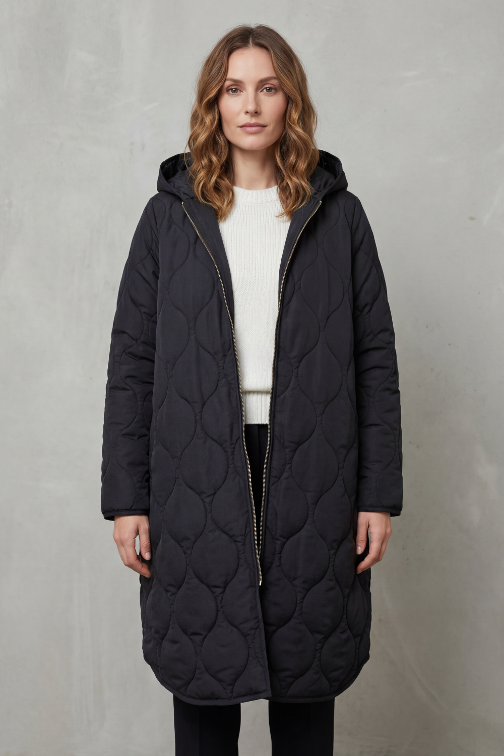 Modella indossa un parka trapuntato lungo con cappuccio, zip frontale e vestibilità rilassata, abbinato a un maglione chiaro._1