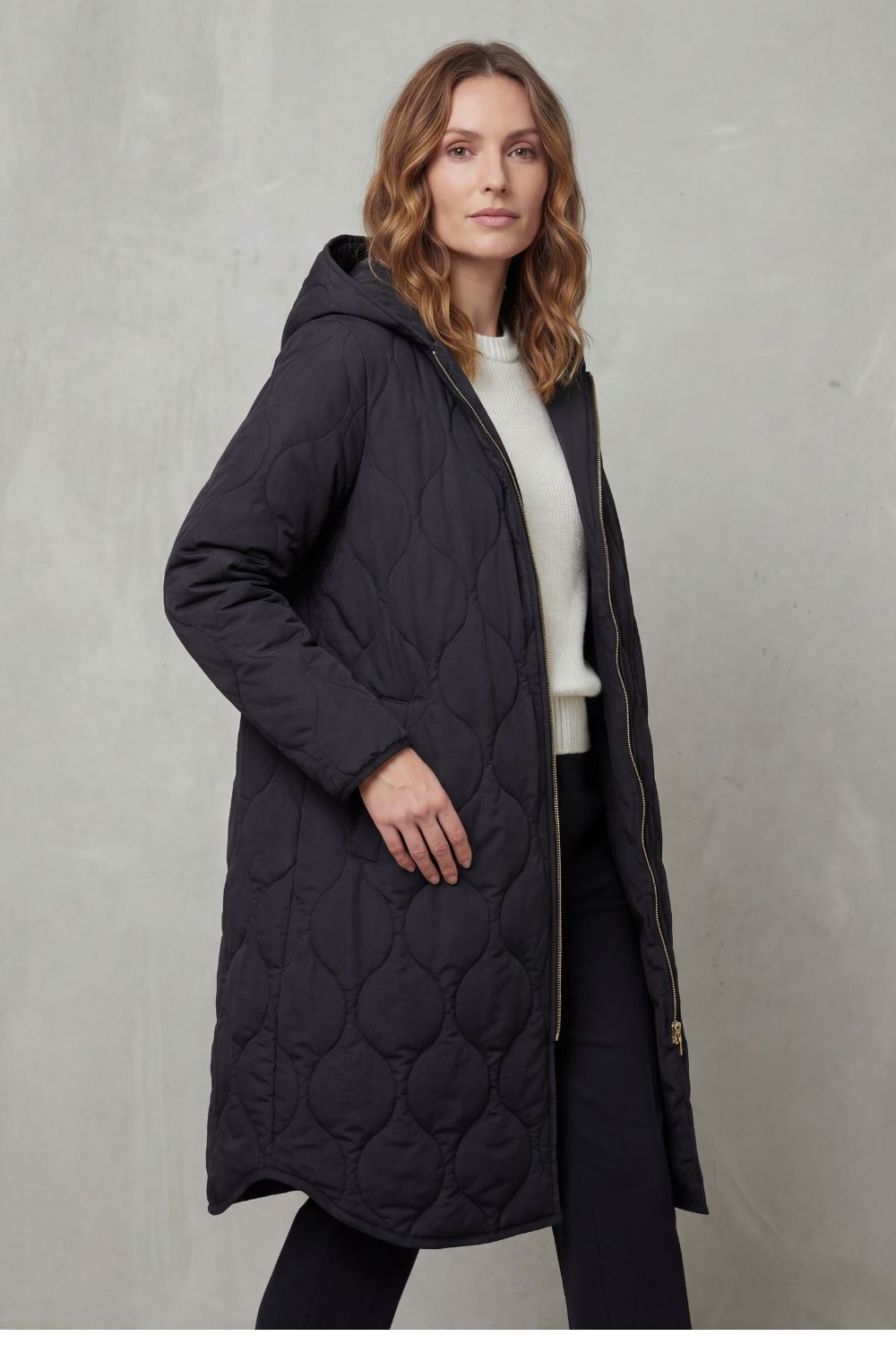 Modella indossa un parka trapuntato lungo con cappuccio, zip frontale e vestibilità rilassata, abbinato a un maglione chiaro._2