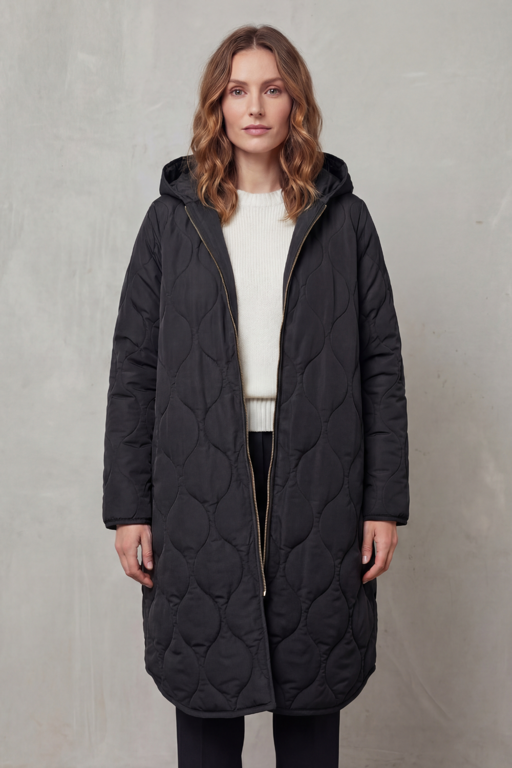 Modella indossa un parka trapuntato lungo con cappuccio, zip frontale e vestibilità rilassata, abbinato a un maglione chiaro._7