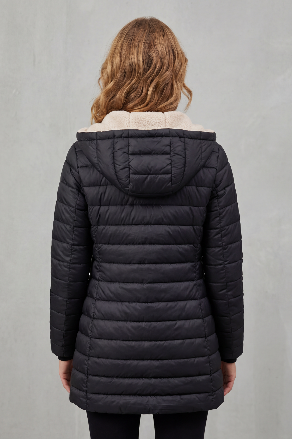 Donna che indossa un piumino imbottito con cappuccio e fodera calda, aperto sul davanti, sopra un maglione beige e pantaloni scuri._3